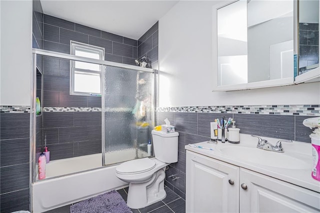 full bathroom with bath / shower combo with glass door, tile walls, vanity, toilet, and tile patterned floors