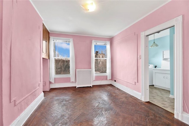 empty room featuring crown molding, baseboards, radiator heating unit, and washer / clothes dryer
