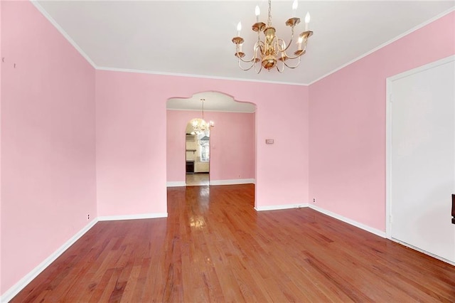 empty room with wood finished floors, arched walkways, an inviting chandelier, crown molding, and baseboards