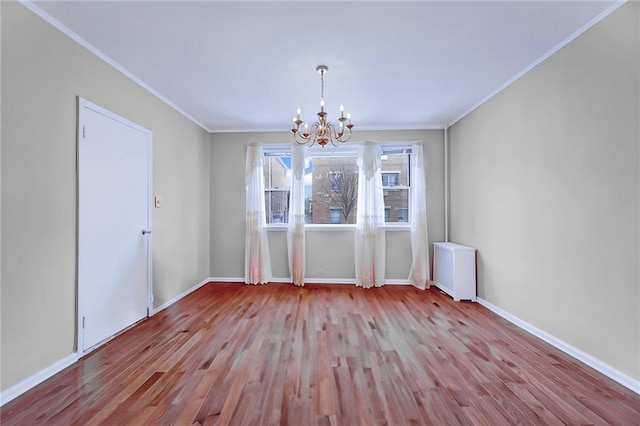 unfurnished dining area featuring baseboards, wood finished floors, a notable chandelier, and crown molding