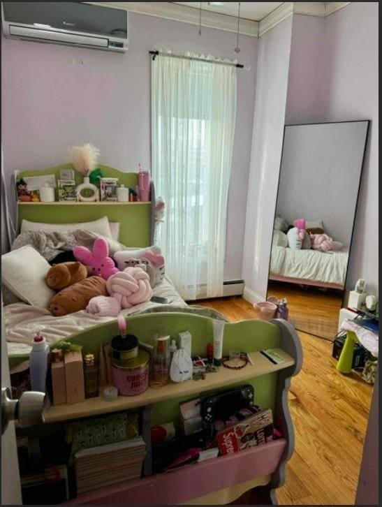 bedroom with hardwood / wood-style flooring, ornamental molding, and a wall unit AC