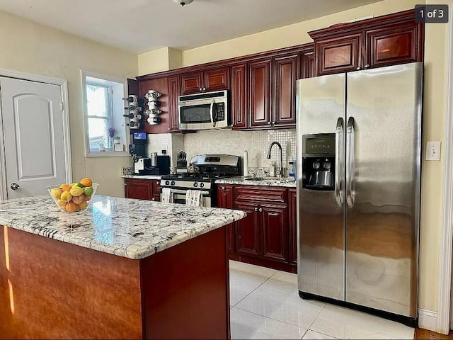 kitchen featuring sink, light tile patterned floors, stainless steel appliances, light stone countertops, and a kitchen island