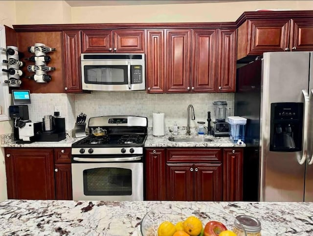 kitchen featuring tasteful backsplash, light stone countertops, appliances with stainless steel finishes, and sink