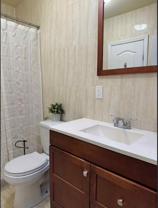 bathroom featuring vanity, tile walls, and toilet