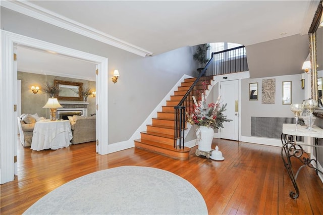 entryway with hardwood / wood-style floors, stairway, baseboards, a fireplace, and crown molding