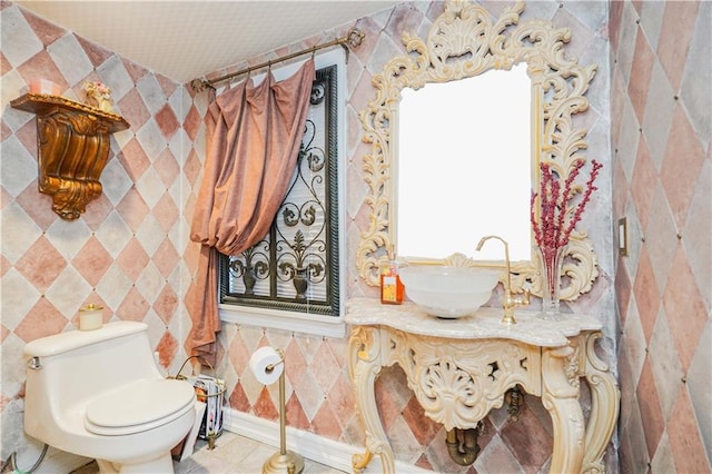 half bath featuring tile walls, toilet, tile patterned floors, and a sink