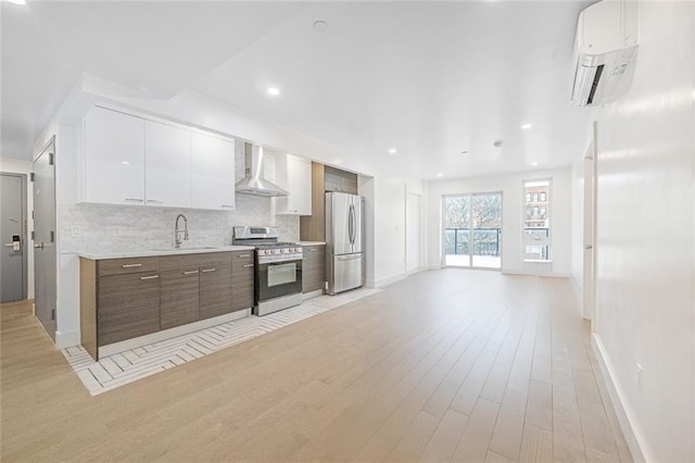 kitchen with white cabinetry, tasteful backsplash, a wall mounted AC, stainless steel appliances, and wall chimney range hood