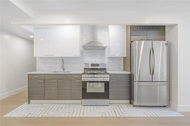 kitchen with wall chimney range hood, stainless steel appliances, a sink, baseboards, and white cabinetry