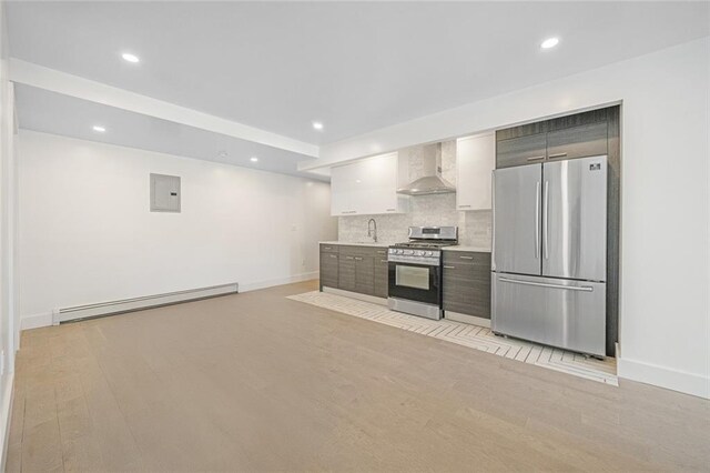 kitchen with sink, baseboard heating, appliances with stainless steel finishes, light hardwood / wood-style floors, and wall chimney exhaust hood