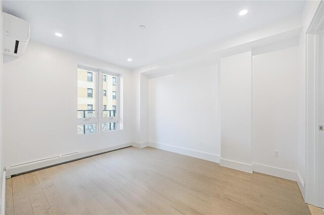 spare room with a baseboard heating unit, a wall unit AC, and light wood-type flooring