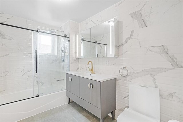 full bathroom featuring toilet, vanity, bath / shower combo with glass door, and tile walls