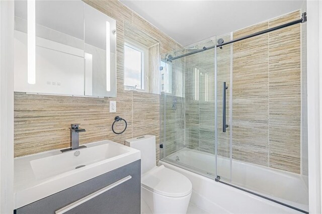 full bathroom featuring tile walls, vanity, bath / shower combo with glass door, and toilet