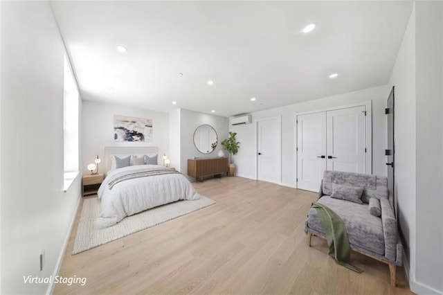 bedroom featuring multiple closets, a wall unit AC, and light hardwood / wood-style floors