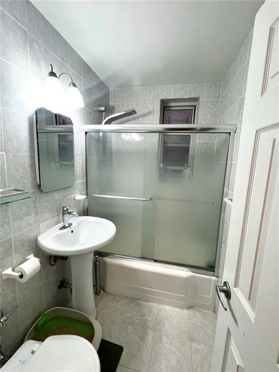 bathroom featuring tasteful backsplash, tile walls, shower / bath combination with glass door, toilet, and tile patterned floors