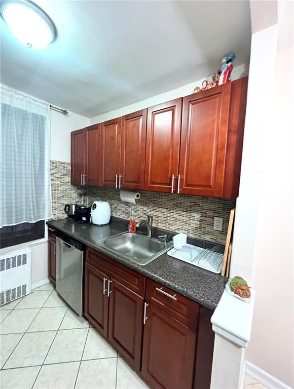 kitchen with radiator, sink, backsplash, light tile patterned flooring, and stainless steel dishwasher