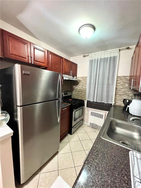 kitchen featuring light tile patterned flooring, sink, radiator, stainless steel appliances, and backsplash