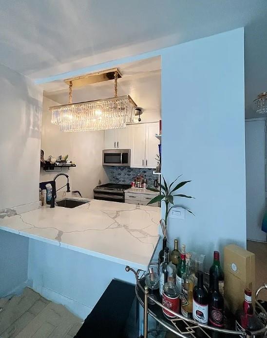 kitchen with appliances with stainless steel finishes, sink, white cabinets, decorative backsplash, and kitchen peninsula