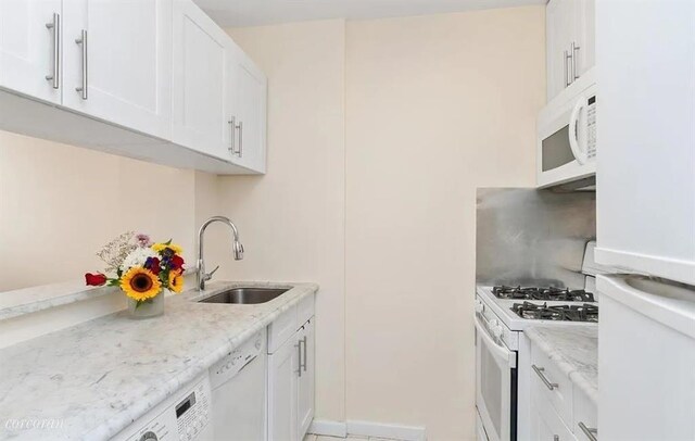 kitchen featuring sink, white appliances, washer / clothes dryer, light stone countertops, and white cabinets