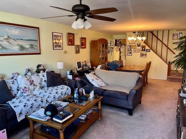 carpeted living room featuring ceiling fan with notable chandelier