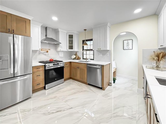 kitchen featuring appliances with stainless steel finishes, white cabinetry, sink, hanging light fixtures, and wall chimney range hood