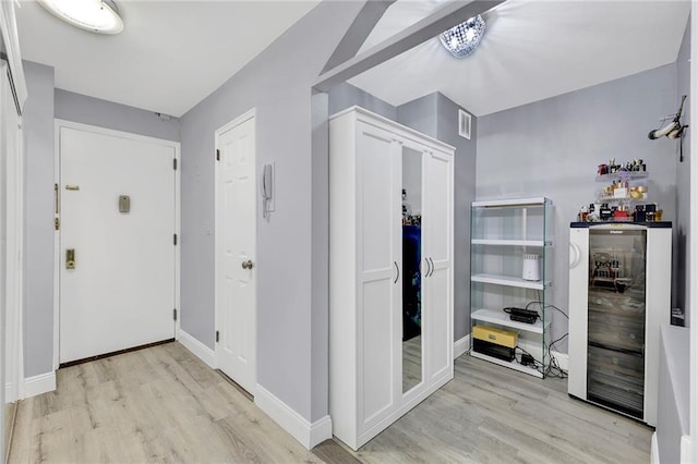 corridor with light wood-style floors, visible vents, wine cooler, and baseboards