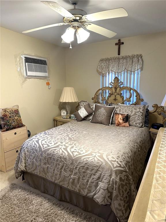 carpeted bedroom featuring an AC wall unit and ceiling fan