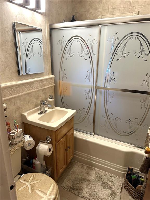 bathroom featuring vanity, combined bath / shower with glass door, tile walls, and tile patterned floors