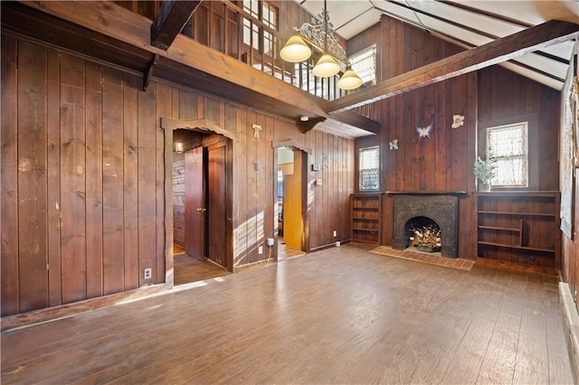 unfurnished living room featuring beam ceiling, a chandelier, hardwood / wood-style floors, and wooden walls