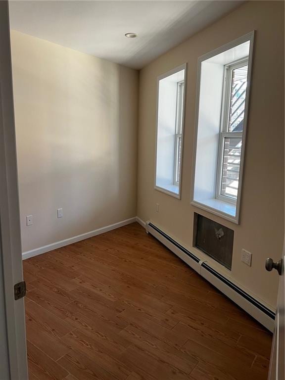 spare room featuring baseboard heating and dark hardwood / wood-style flooring