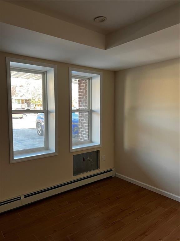 unfurnished room with a baseboard radiator, dark wood-type flooring, and a tray ceiling