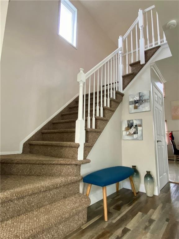 stairs with baseboards, wood finished floors, and a towering ceiling