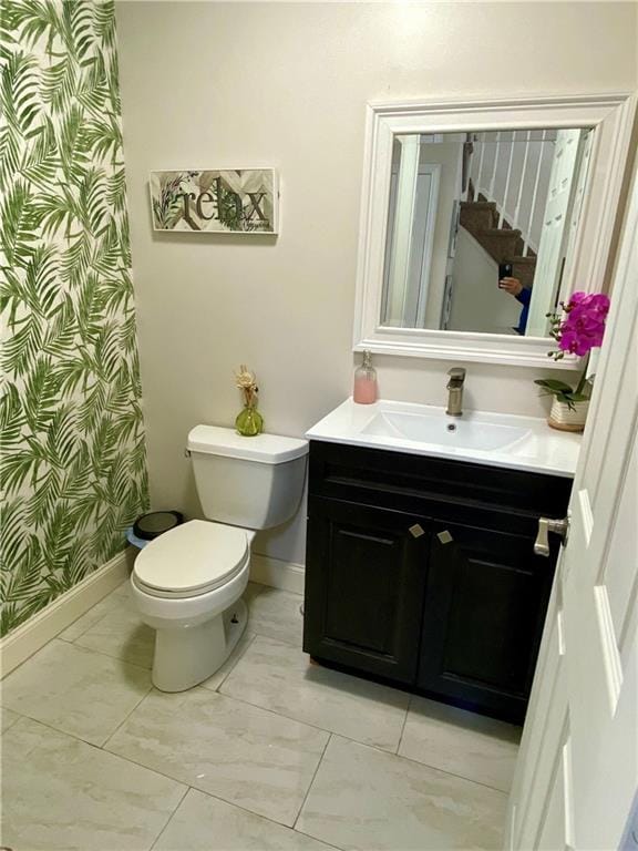 bathroom featuring baseboards, wallpapered walls, toilet, and vanity