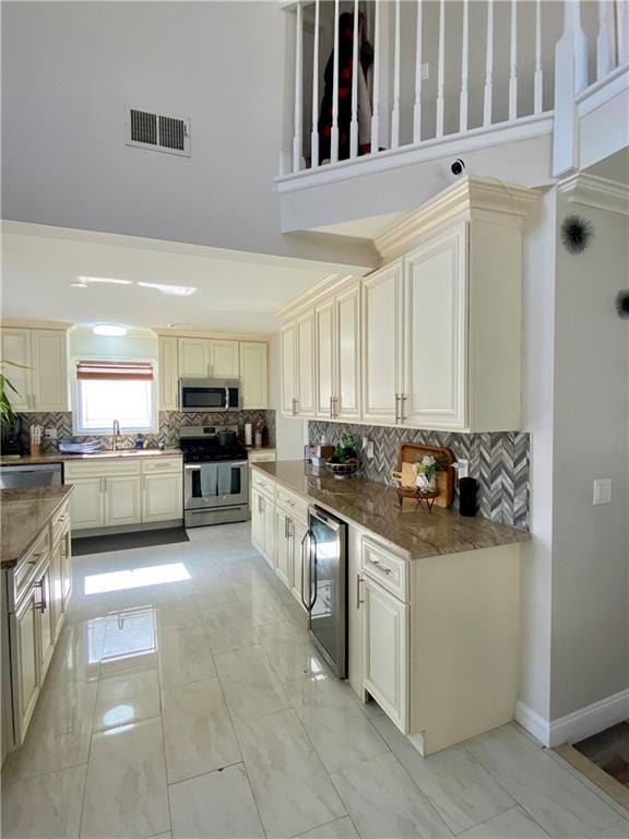 kitchen with a high ceiling, decorative backsplash, wine cooler, visible vents, and appliances with stainless steel finishes