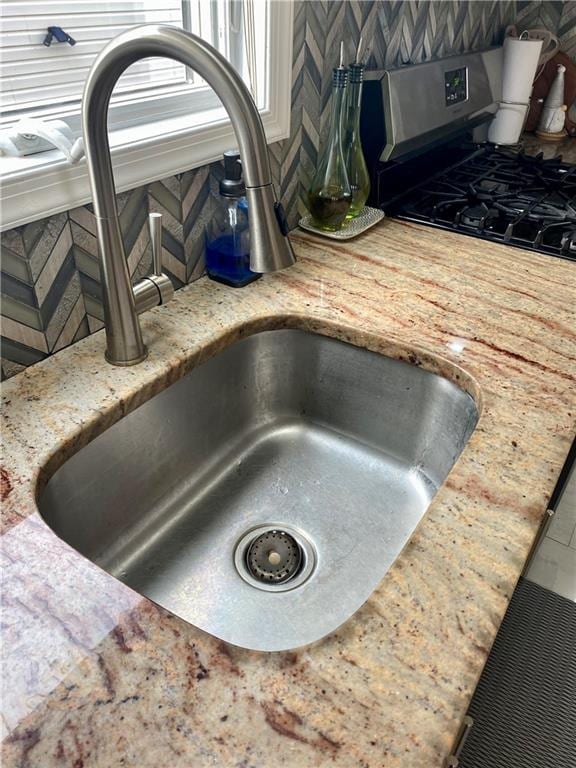 interior details with stainless steel gas range, light stone counters, decorative backsplash, and a sink