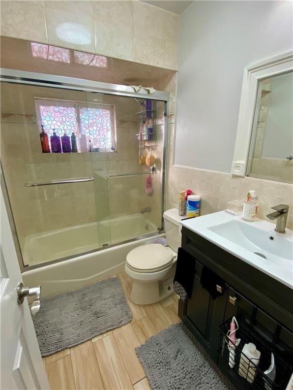 full bathroom with shower / bath combination with glass door, tile walls, vanity, toilet, and wood finished floors
