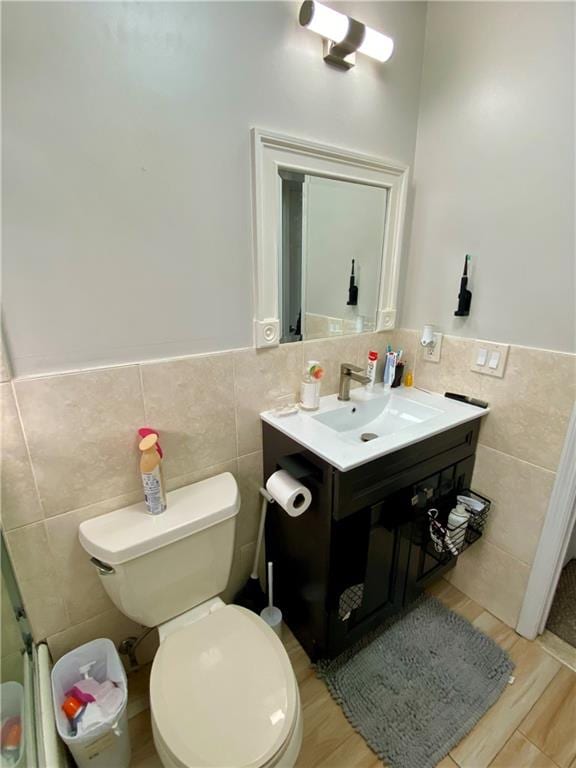 bathroom featuring a wainscoted wall, toilet, tile walls, wood finished floors, and vanity