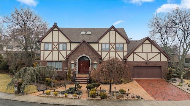 english style home with brick siding, an attached garage, stucco siding, and decorative driveway