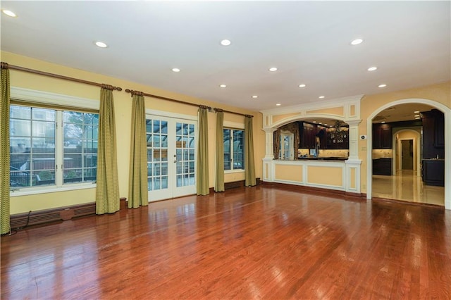 unfurnished living room with arched walkways, wood finished floors, recessed lighting, and french doors