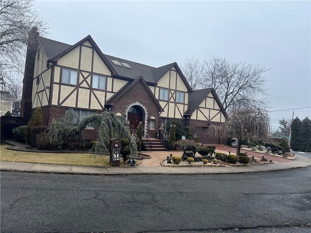 english style home featuring brick siding, a chimney, and stucco siding