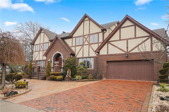 tudor house featuring roof with shingles, stucco siding, decorative driveway, brick siding, and a garage