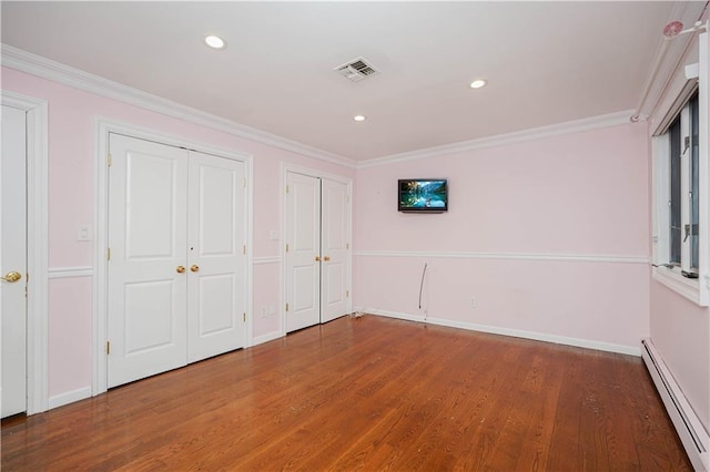 unfurnished bedroom with multiple closets, wood finished floors, visible vents, baseboards, and a baseboard radiator