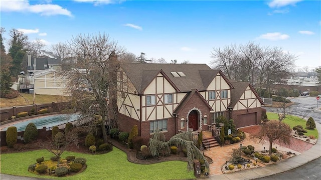 english style home featuring a garage, a shingled roof, a front lawn, and stucco siding
