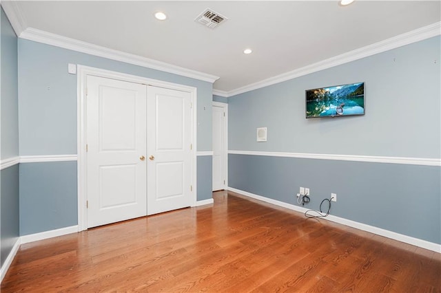 unfurnished bedroom featuring baseboards, visible vents, wood finished floors, a closet, and crown molding