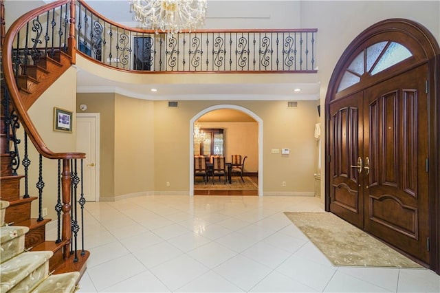 tiled entrance foyer with stairway, a towering ceiling, arched walkways, baseboards, and a notable chandelier