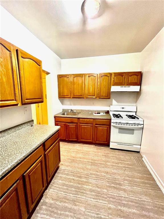 kitchen with light stone counters, sink, light hardwood / wood-style floors, and white gas stove