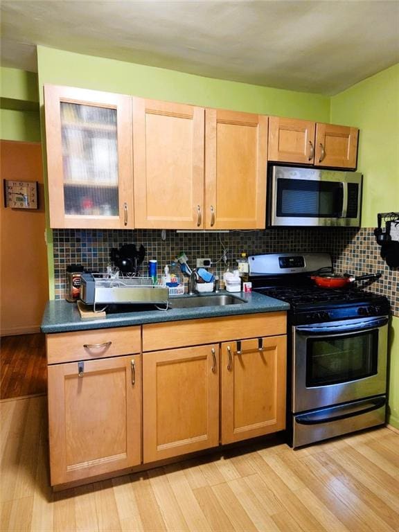 2400 E 3rd St Unit 406, Brooklyn, NY 11223 - kitchen featuring stainless steel appliances, backsplash, light wood-type flooring, dark countertops, and a sink
