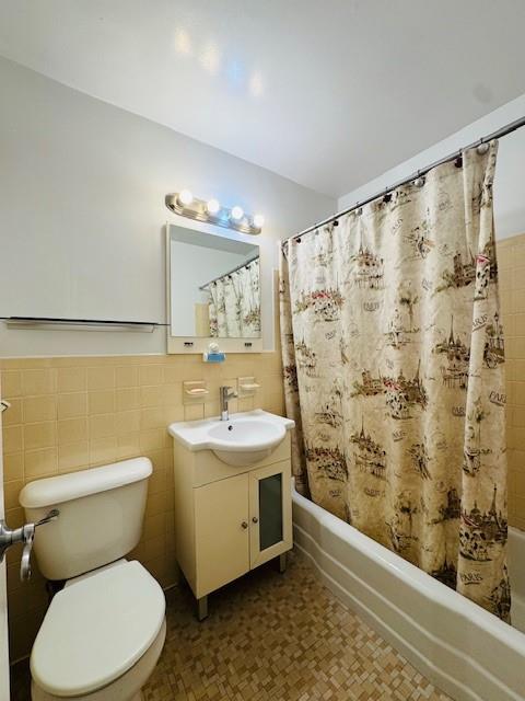 full bath featuring shower / tub combo, toilet, a wainscoted wall, vanity, and tile walls