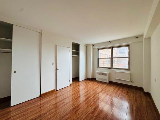 unfurnished bedroom with radiator, two closets, and wood finished floors