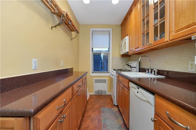 kitchen with radiator heating unit, sink, dark stone countertops, decorative backsplash, and white appliances