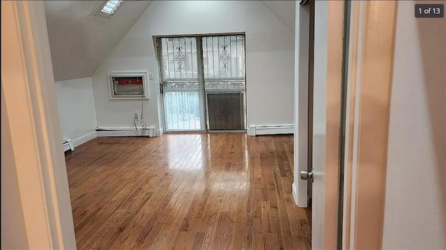 additional living space with lofted ceiling, a wall mounted air conditioner, hardwood / wood-style flooring, and baseboard heating